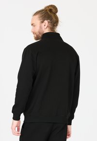 Sort sweatshirt med høj krave og ribbede manchetter. Har en glat tekstur og en afslappet pasform, set fra en side-bagud-udsigt.