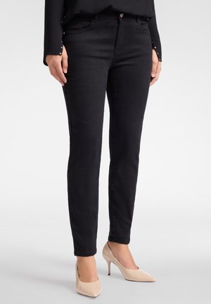 Schwarze Skinny Jeans aus Denim, mit einem klassischen Fünf-Taschen-Design und einem dezenten Glanz. Kombiniert mit nudefarbenen High Heels.