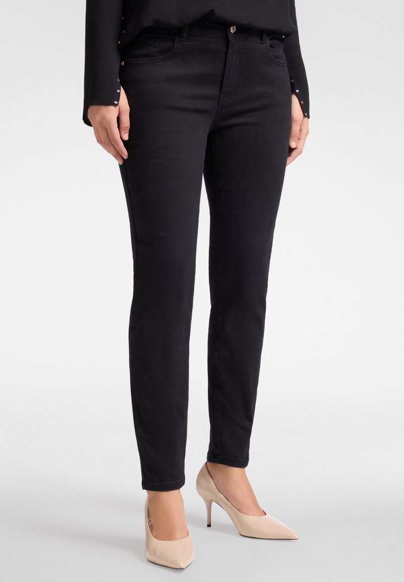 Mustat skinny-farkut, joissa on klassinen viiden taskun muotoilu ja hienostunut kiilto. Yhdistettynä nude-väreihin korkokenkiin.