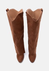 Καφέ σουέντ μπότες πάνω από το γόνατο με λεία υφή, μυτερή μύτη και χωρισμένο πάνω άκρο. Διαθέτουν φερμουάρ στο εσωτερικό για εύκολη εφαρμογή.