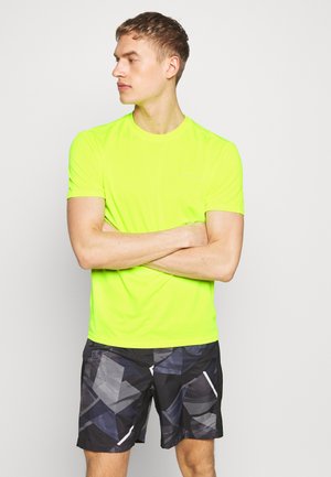 Neon gul kortærmet træningsskjorte parret med sorte shorts med geometrisk mønster og hvide accenter. Glat, letvægtsstof.