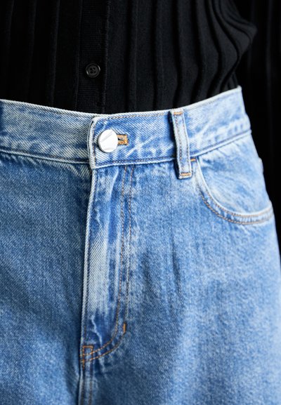 Hellblaue Jeans mit hoher Taille, ausgestattet mit einem silbernen Knopf, orangefarbener Naht und einer leicht abgetragenen Textur.