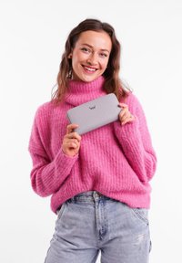 Gray wallet with embossed logo, dotted pattern; model in a fuzzy pink sweater, blue jeans, holds the wallet up, smiling against a white background.