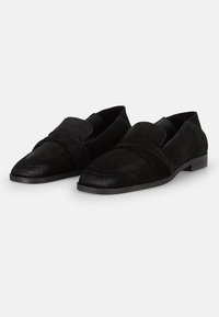 Black suede loafers featuring a curved front design, stitched detailing, and a flat rubber sole. Accented with a wide fabric strap.