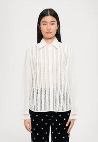 Balta palaidinė su vertikaliomis nėrinio juostelėmis, klasikinio kirpimo apykaklė ir ilgomis rankovėmis. Rankovių apačioje yra banguoto nėrinio apdaila. Elegantiška ir lengva medžiaga.