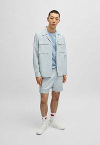 Lyseblå stribet jakke med to forlommer, parret med matchende shorts. Båret over en ensfarvet blå t-shirt og hvide sneakers.