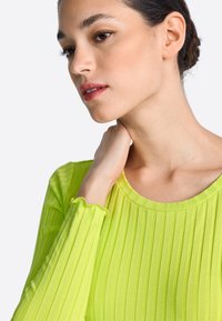 Citromzöld bordázott hosszú ujjú felső, kerek nyakkivágással és fodros mandzsettákkal, könnyű, rugalmas anyagból készült.