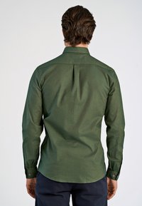 Camisa verde de manga larga con cuello, pliegue en la espalda y puños abotonados. Elaborada en una tela texturizada con un acabado suave.