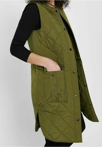 Pikowana oliwkowozielona kamizelka z zapięciem na guziki z przodu, bocznymi rozcięciami i naszywaną kieszenią po lewej stronie. Tkanina o fakturze i prosty design.