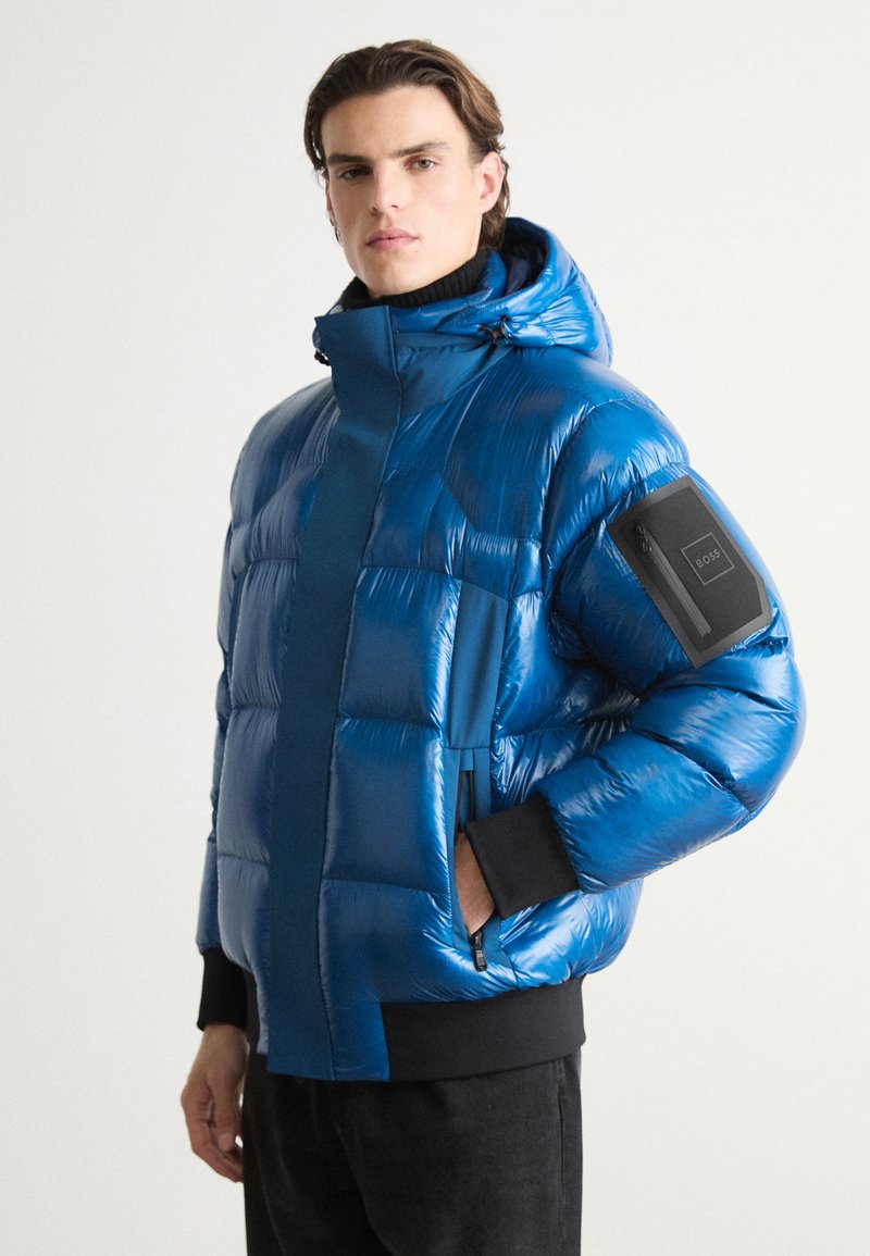 Pūdera jaka spožā elektriski zilenā krāsā ar augstu apkakli, ar rāvējslēdzēja kabatām un melniem akcentiem uz piedurknēm. Tekstūras, quilted dizains.