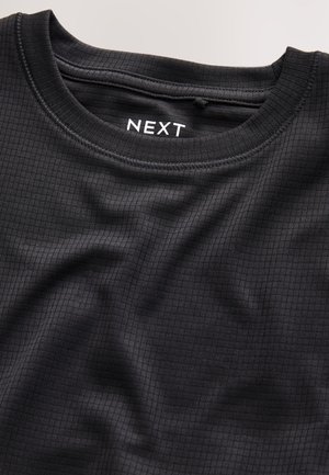Mustast tekstuuriga materjalist lühikeste varrukatega T-särk ruudustikuga mustriga, ümmarguse kaelusega ja sildiga, millel on kiri "NEXT".