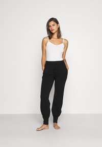 Zwarte sweatpants met een trekkoord in de taille en geribde boorden, gecombineerd met een witte cami-top. Glad textuur, ontspannen pasvorm, geen patronen.