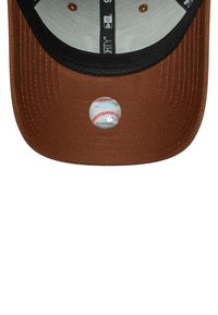Braune Baseballmütze mit schwarzschirm. Vorn ist ein runder Aufkleber mit einem Baseballgrafik angebracht. Innen ist sie mit grauem Stoff gefüttert.