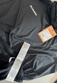 Indumento in pile nero Mammut con etichette di cura e cartellino del prezzo allegato con dettagli del prodotto.