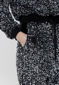 Błyszcząca czarna i srebrna tkanina z cekinami, luźny krój, z elastycznym paskiem i czarnym guzikiem na kieszeni.