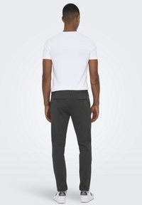 Chemise blanche à manches courtes associée à un pantalon gris à rayures et des baskets avec des accents verts. La coupe est décontractée et contemporaine.