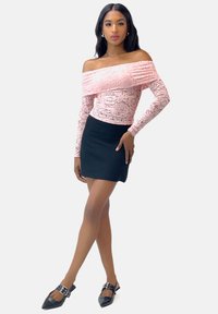 Off-the-shoulder lyserød blonde top med tekstureret detaljer, parret med en tætsiddende sort mini nederdel. Modellen har sorte spidse flade sko på med hardware-accenter.