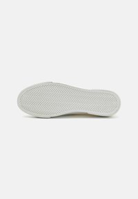 Sole of a shoe, white rubber with herringbone tread pattern, smooth edges, slightly rounded toe, flat profile.