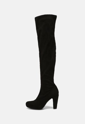 Botte femme noire en daim montant jusqu’au genou avec bout arrondi et talon haut épais, vue de profil sur fond uni.
