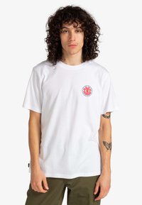 Weißes Baumwoll-T-Shirt mit einem roten Logo auf der linken Brust, lockere Passform, kurze Ärmel und Rundhalsausschnitt.