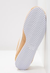 Nike-sneaker med en överdel i beige läder med texturerad yta, vit gummisula med herringbone-mönster.