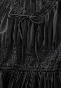 Schwarzes Kleid mit V-Ausschnitt, gerafftem Oberteil und durchgehend strukturierter Textur, mit Bindeband am Ausschnitt und fließendem Rock.