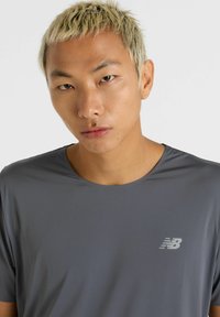 Grå atletisk t-shirt med korte ærmer, lavet af glat stof, med et diskret New Balance-logo på venstre bryst.
