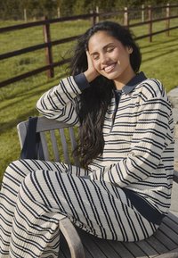 Conjunto de ropa de casa a rayas en crema y azul marino, que incluye una blusa de cuello con mangas largas y pantalones de pierna ancha a juego. Tejido texturizado con un patrón de costura visible.