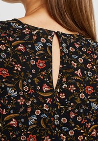 Primer plano de la espalda de una mujer que muestra un vestido floral negro con flores rojas, azules y blancas, y un cierre con botón en forma de ojal en el cuello.