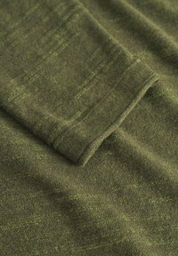 Texturiertes olivgrünes Material mit weicher Oberfläche, das ein dezentes Muster und eine gefaltete Kante zeigt und das gestrickte Design betont.