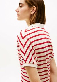Gestreiftes Poloshirt in Creme mit roten horizontalen Linien. Verfügt über einen Umlegekragen und gerippte Bündchen, mit einem kleinen Akzentlogo an einem Ärmel.