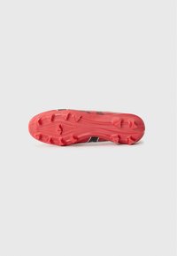 Zwarte en rode sport schoen zool met duidelijke noppenpatronen, gladde rode rubber en een gestructureerd oppervlak voor grip.