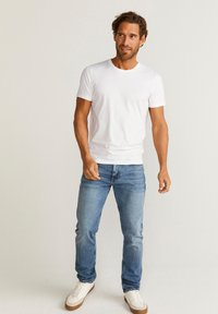 Hvid bomulds T-shirt med rund halsudskæring, parret med lyseblå denimbukser og hvide sneakers med brune såler.