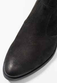 Czarne zamszowe botki za kostkę o eleganckim fasonie, z ostro zakończonym noskiem, elastycznymi bocznymi panelami oraz teksturowaną powierzchnią. Trwała gumowa podeszwa.