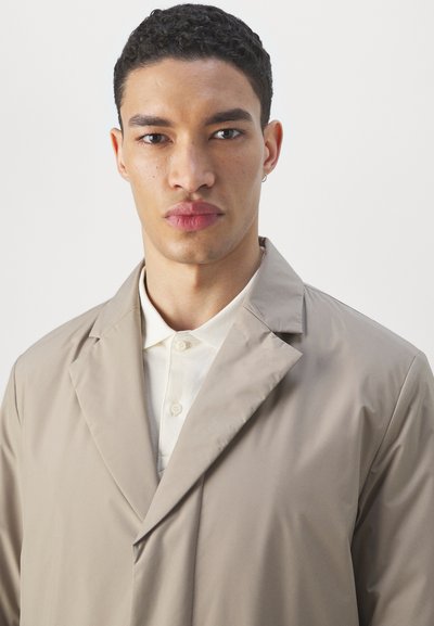 Beige overcoat with a smooth texture, single-breasted design, and a wide lapel, paired with a light-colored collar shirt.