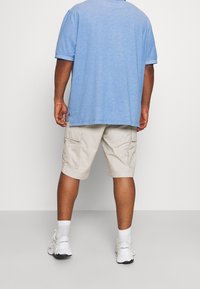 Camisa de manga corta azul clara, de corte relajado, combinada con pantalones cortos de carga beige con bolsillos laterales, calcetines blancos y zapatillas deportivas.