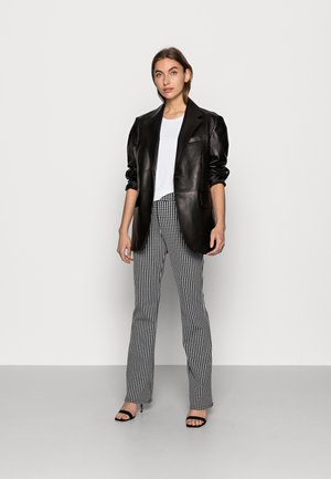 Schwarze Lederblazer, tailliert mit scharfen Revers. Darunter ein weißes T-Shirt, kombiniert mit schwarz-weißen karierten Hosen. Schwarze Absatzsandalen.