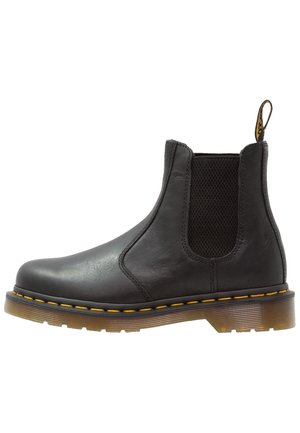 Bottines Chelsea en cuir noir avec panneaux latéraux élastiques, couture jaune le long de la semelle, semelle translucide crantée et bandeau en tissu à l'arrière.