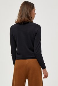 Schwarzer Strickpullover mit langen Ärmeln und rundem Ausschnitt, kombiniert mit braunen Weiten Hosen. Glatte Textur, gerippte Saumdetails.