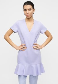Φόρεμα λιλά με κοντά μανίκια, ντεκολτέ σε σχήμα V και φαρδιά τελείωμα. Ομαλή υφή, απλός σχεδιασμός και εφαρμοστή σιλουέτα. Χωρίς εμφανή σχέδια ή διακοσμητικά στοιχεία.