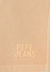 Tkanina boje breskve s mekim teksturom, s uzdignutim logotipom "PEPE JEANS" u usklađenoj nijansi na donjem dijelu.