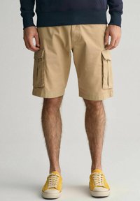 Beige cargo shorts med to sidelommer med klap og en løs pasform, parret med gule sneakers og en marineblå sweatshirt.