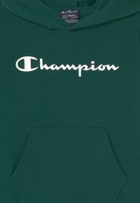 Sudadera verde Champion con texto del logo en blanco en el pecho y un bolsillo canguro en la parte frontal, la etiqueta muestra la talla 2X pequeña.