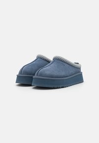 Blue suede clogs with a thick platform sole and a textured knitted trim along the upper edge. Features subtle brand logo on the side.