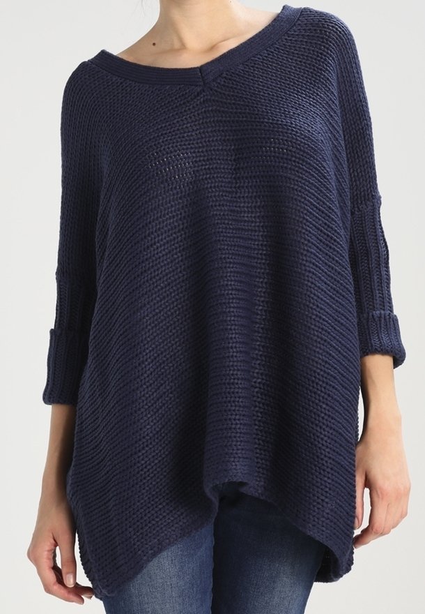 Femme portant un pull ample en tricot bleu marine à manches trois-quarts et col bateau, assorti à un jean bleu.