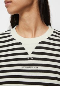 Felpa a righe bianco e nero con collo a coste, dettaglio a forma di V sul colletto e piccolo logo ricamato sul davanti.