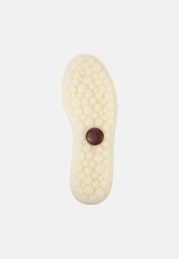 Insole di colore bianco con texture a bolle, dalla forma arrotondata, con un logo circolare marrone al centro. Design leggero e flessibile.