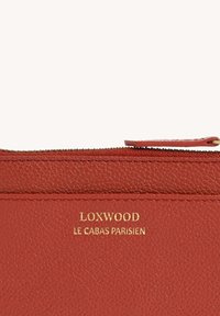 Portefeuille en cuir rouge avec une finition texturée. Présente un logo doré "LOXWOOD" et "LE CABAS PARISIEN" à l'extérieur. Fermeture éclair en haut.
