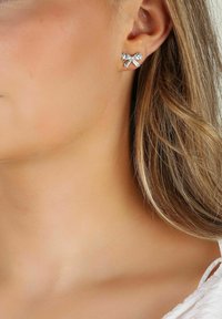Silverfärgade stiftörhängen formade som en rosett med klara rhinestones, med en polerad yta och en enkel, elegant design.