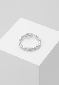 Sølvvridd ring med en glatt, polert overflate og sammenflettet design. Vist på en ren hvit pedestal.